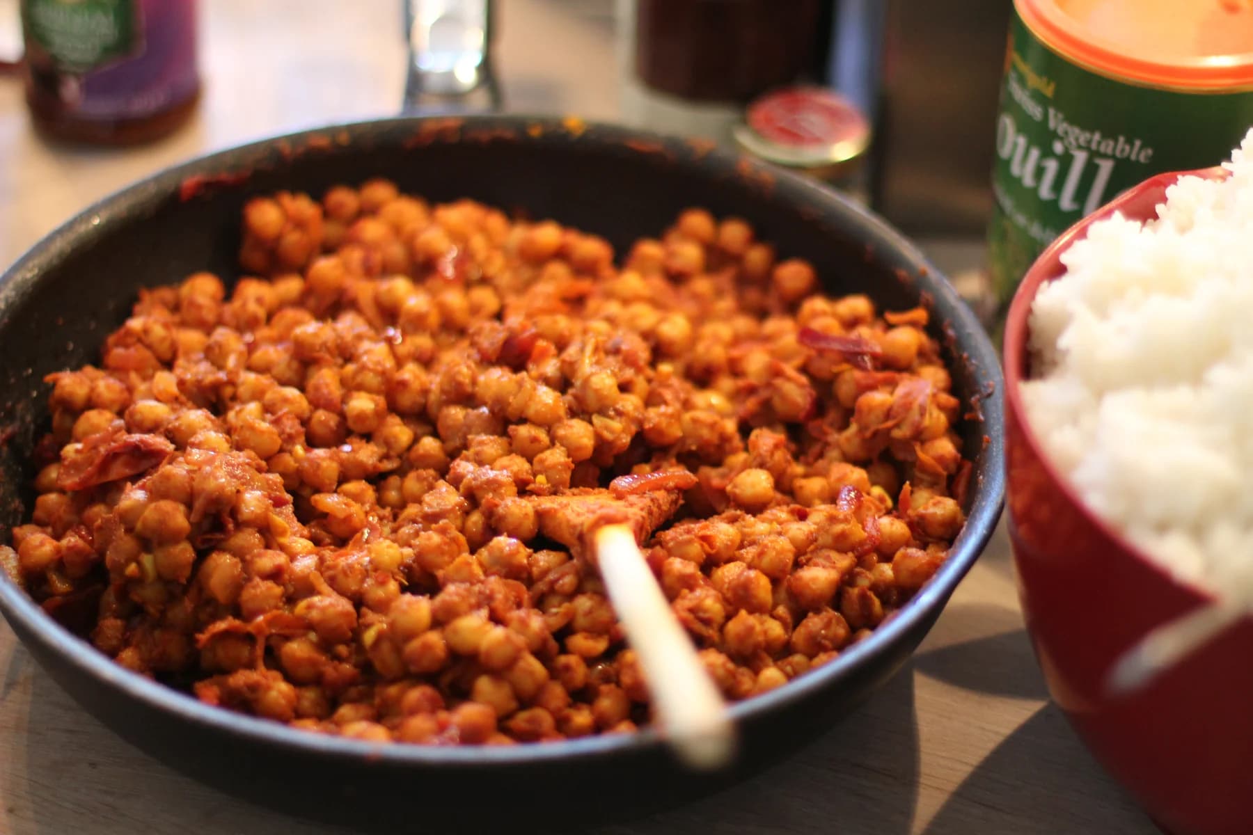 Home-cooked chickpea curry in a skillet beside a bowl of rice