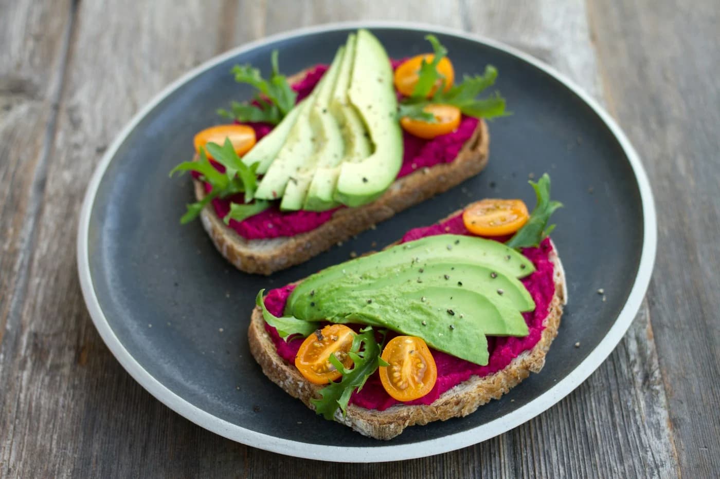 Avocado toast with tomatoes and rocket on a dark ceramic plate