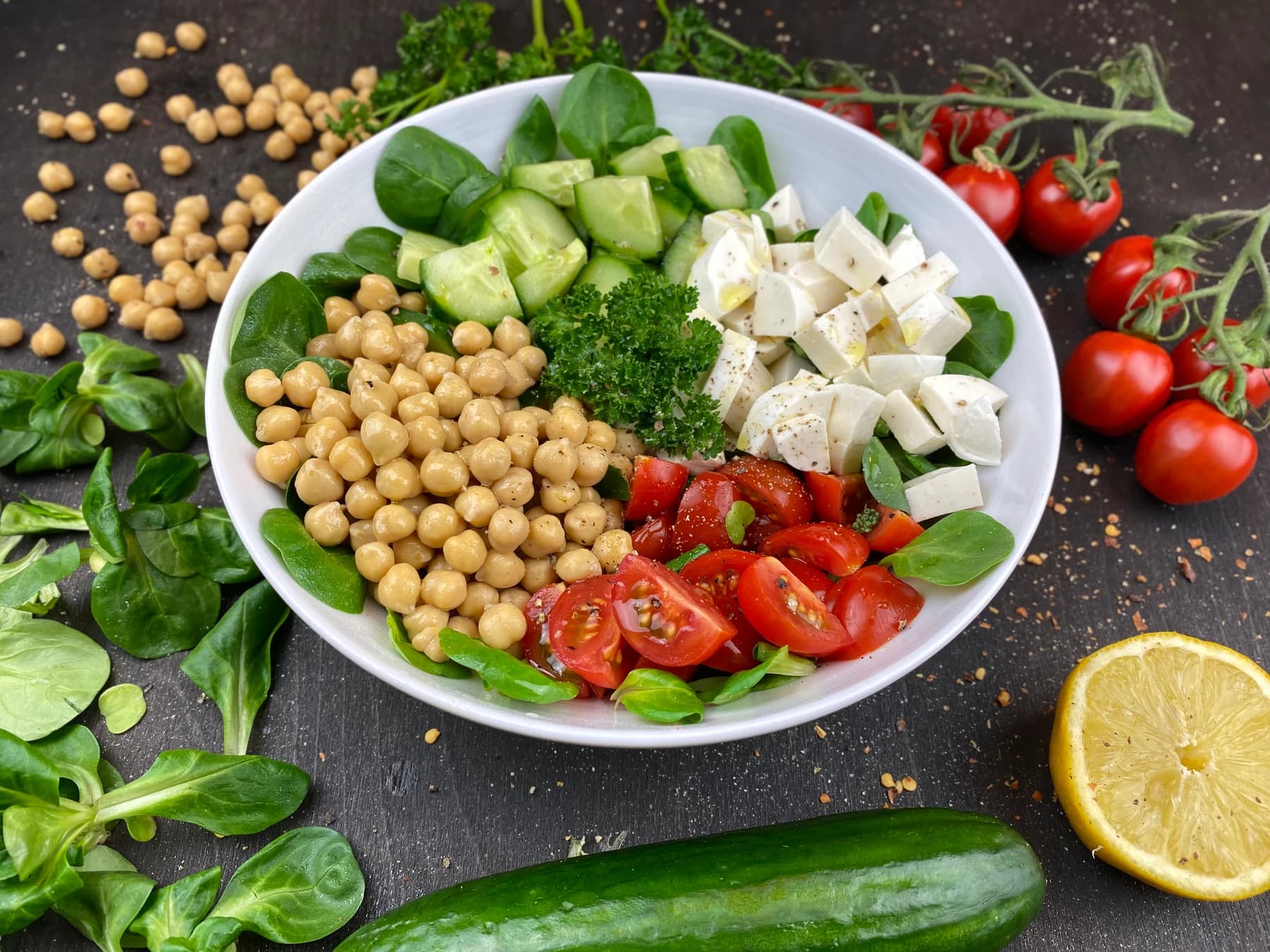 A bowl of chickpeas, cucumber, tomatoes, greens and white cheese