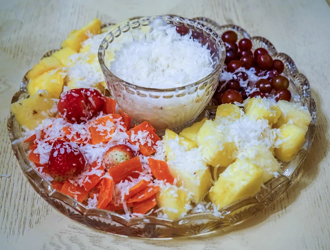 A glass platter of grapes, strawberries and pineapple with shredded coconut