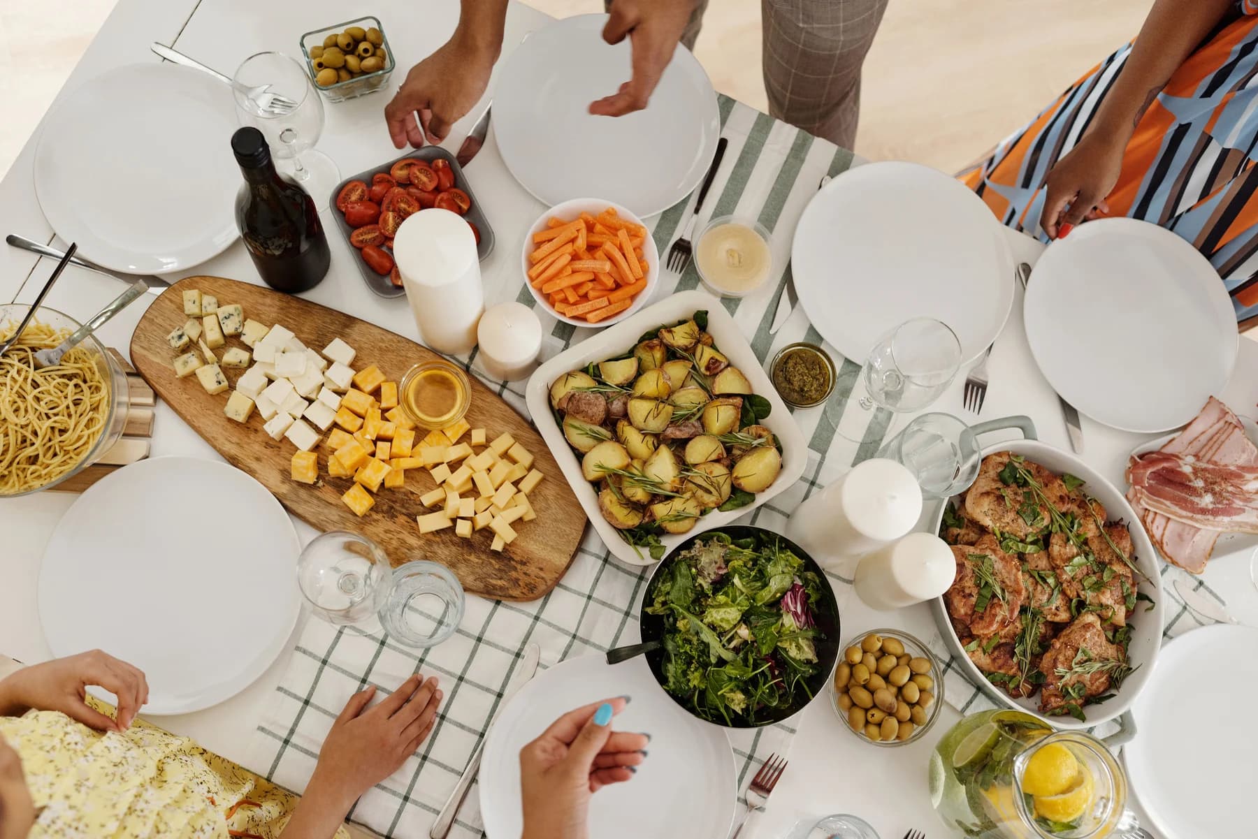 An overhead view of hands sharing vegetables and cheese around a table